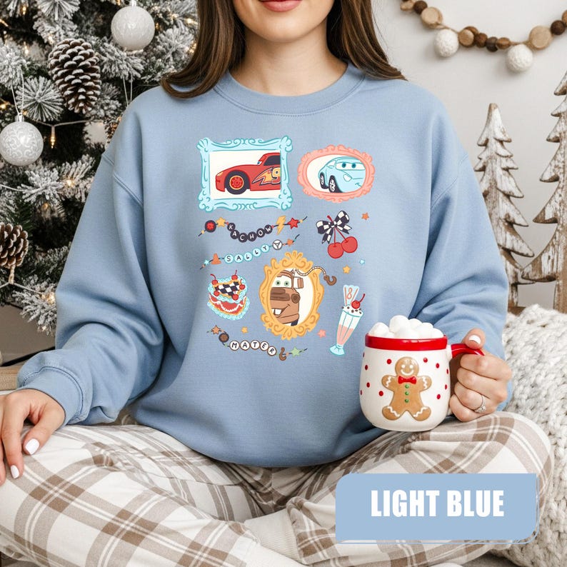 Puede incluir: Una sudadera de cuello redondo en color azul claro con un estampado gr&aacute;fico de personajes de la pel&iacute;cula Cars, incluyendo a Rayo McQueen, Sally y Mate en marcos ornamentados, junto a cerezas, un batido y el texto Kachow, Sally y Mater.