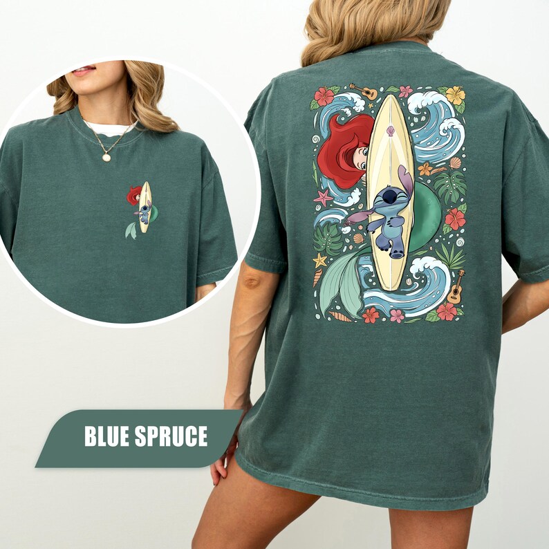 May include: A blue spruce t-shirt featuring a small graphic on the front left chest and a large back graphic of a blue alien character on a surfboard, surrounded by red hair, tropical flowers, green leaves, seashells, and blue ocean waves.