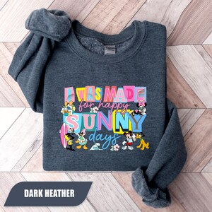 May include: Dark heather gray sweatshirt with the text "I WAS MADE for happy SUNNY days" in colorful block letters. Disney characters like Mickey Mouse, Donald Duck, and Minnie Mouse are featured in the design. The words "DARK HEATHER" are at the bottom.
