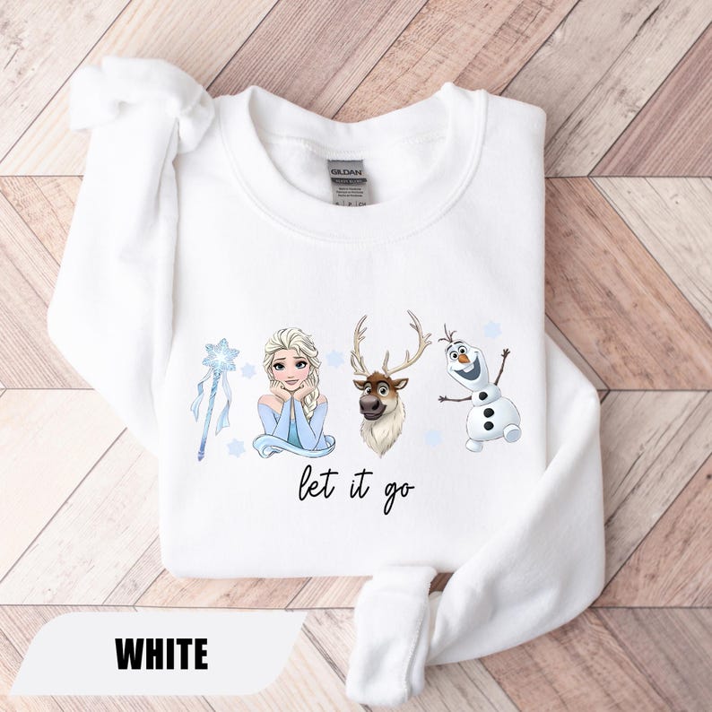 May include: White sweatshirt featuring Elsa, a reindeer, and Olaf from Frozen, with a blue wand and stars. The phrase "let it go" is written in black script. The word "WHITE" is printed at the bottom.