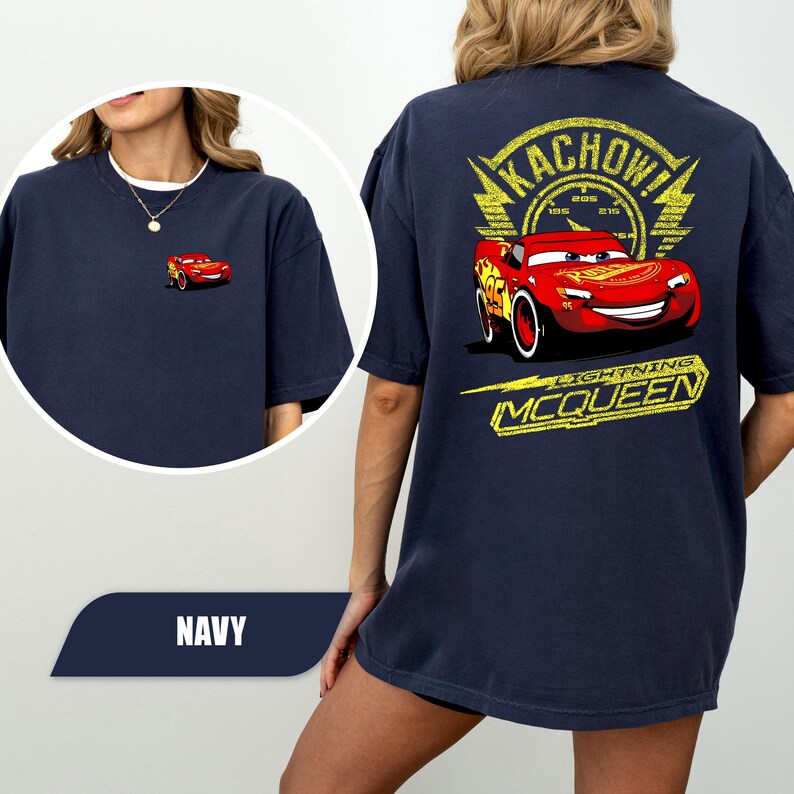 May include: A navy blue t-shirt featuring a small graphic of the red race car Lightning McQueen on the front left chest. The back displays a large yellow graphic with the text KACHOW and LIGHTNING MCQUEEN surrounding the red race car.