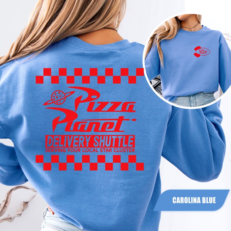 May include: A Carolina blue crewneck sweatshirt featuring a red graphic on the back with a checkered border, the text Pizza Planet, DELIVERY SHUTTLE, and SERVING YOUR LOCAL STAR CLUSTER. A smaller red Pizza Planet logo is printed on the front chest.