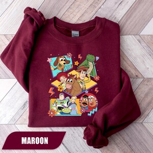 Puede incluir: Sudadera granate con un gr&aacute;fico colorido de personajes de Toy Story. El dise&ntilde;o incluye a Woody, Buzz Lightyear y otros personajes, con la palabra "MAROON" en la parte inferior. Un dise&ntilde;o divertido y vibrante.