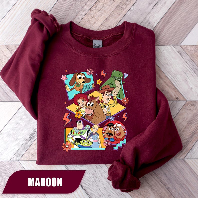 Puede incluir: Sudadera granate con un gr&aacute;fico colorido de personajes de Toy Story. El dise&ntilde;o incluye a Woody, Buzz Lightyear y otros personajes, con la palabra "MAROON" en la parte inferior. Un dise&ntilde;o divertido y vibrante.