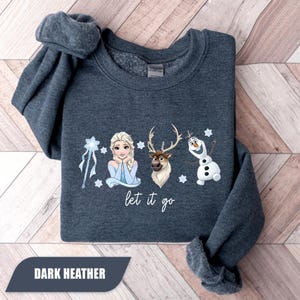May include: Dark heather gray sweatshirt featuring Elsa, Sven, and Olaf from Frozen. The phrase "let it go" is written below the characters. The sweatshirt has rolled sleeves and the words "DARK HEATHER" are printed on a dark rectangle.