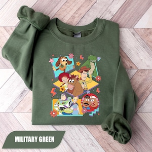 Puede incluir: Sudadera verde militar con un gr&aacute;fico colorido de personajes de Toy Story, incluyendo a Woody y Buzz Lightyear. El dise&ntilde;o est&aacute; enmarcado. La sudadera tiene cuello redondo y mangas largas.