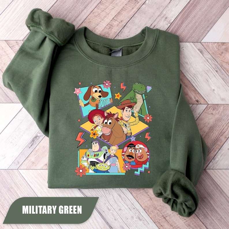 Puede incluir: Sudadera verde militar con un gr&aacute;fico colorido de personajes de Toy Story, incluyendo a Woody y Buzz Lightyear. El dise&ntilde;o est&aacute; enmarcado. La sudadera tiene cuello redondo y mangas largas.