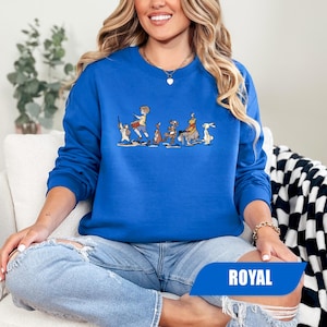 May include: Royal blue sweatshirt featuring a cartoon illustration of characters in a line. The graphic includes a drummer, kangaroo, tiger, and rabbit. The word "ROYAL" is printed on a blue banner at the bottom.
