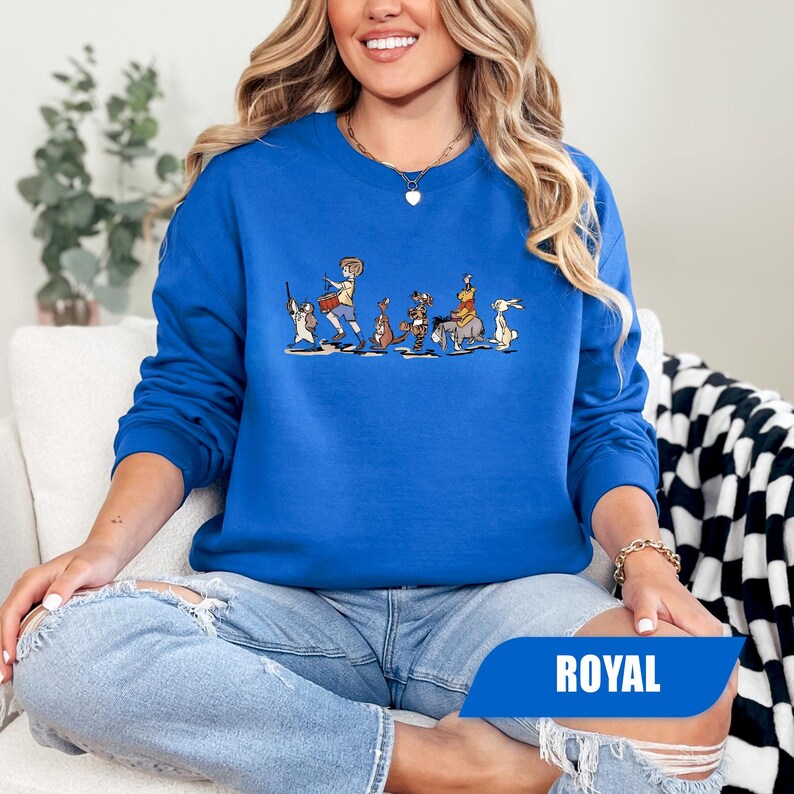 May include: Royal blue sweatshirt featuring a cartoon illustration of characters in a line. The graphic includes a drummer, kangaroo, tiger, and rabbit. The word "ROYAL" is printed on a blue banner at the bottom.