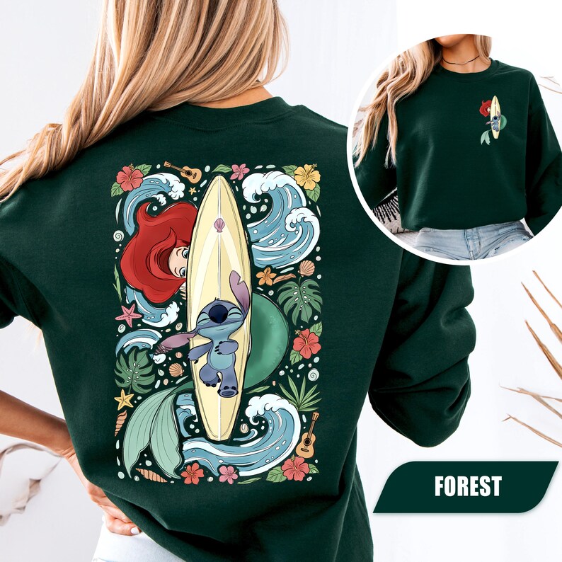 May include: A dark green crewneck sweatshirt featuring a large graphic on the back of a blue alien character on a surfboard, a red-haired mermaid, tropical flowers, waves, and ukuleles. A smaller matching graphic is on the front left chest.