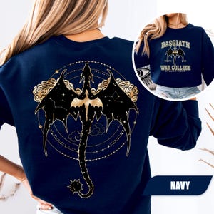 May include: Navy blue sweatshirt featuring a gold and black dragon design on the back. The dragon is surrounded by constellations and clouds. The front of the sweatshirt has the text "BASGIATH FOURTH WING WAR COLLEGE DRAGON RIDER" in gold.