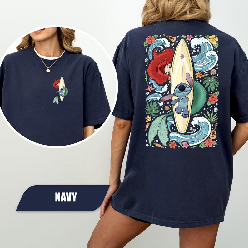 May include: A navy blue t-shirt featuring a small graphic on the front left chest and a large graphic on the back. Both graphics depict a blue alien character on a surfboard with a red-haired mermaid, ocean waves, tropical flowers, and a ukulele.