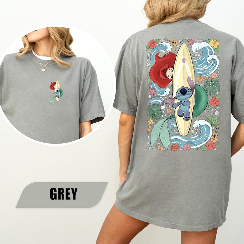May include: A grey short-sleeve t-shirt featuring a small graphic on the front left chest of Stitch on a surfboard. The back of the shirt displays a large, colorful illustration of Stitch and Ariel with a surfboard, waves, flowers, and ukuleles.