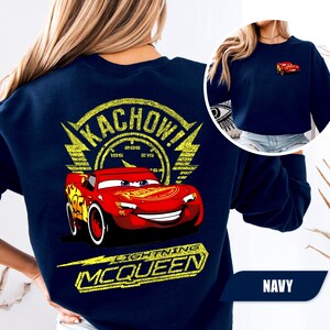 May include: A navy blue sweatshirt featuring a large graphic on the back of the red race car Lightning McQueen with the text KACHOW! and LIGHTNING MCQUEEN in yellow. A smaller version of the red race car is printed on the front left chest area.