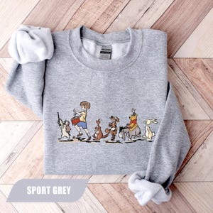 May include: Sport grey sweatshirt featuring a cartoon illustration of a boy leading a parade of animal characters. The boy is playing a drum, and the animals include a dog, kangaroo, tiger, donkey, bear, and rabbit. The text "SPORT GREY" is at the bottom.