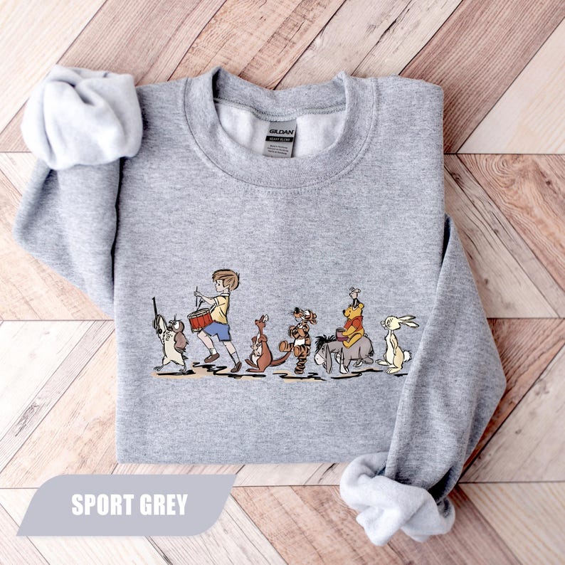 May include: Sport grey sweatshirt featuring a cartoon illustration of a boy leading a parade of animal characters. The boy is playing a drum, and the animals include a dog, kangaroo, tiger, donkey, bear, and rabbit. The text "SPORT GREY" is at the bottom.