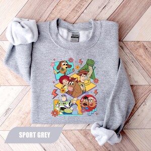 Puede incluir: Sudadera gris deportiva con un dise&ntilde;o gr&aacute;fico colorido de personajes de la pel&iacute;cula animada Toy Story. El dise&ntilde;o incluye a Woody, Buzz Lightyear y otros personajes. La sudadera tiene mangas largas y cuello redondo.