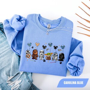 Könnte beinhalten: Carolina-blaues Sweatshirt mit Star Wars-Charakteren, die Ballons halten. Die Grafik zeigt BB-8, Chewbacca, einen Sturmtruppler, Grogu, R2-D2 und Darth Vader. Das Sweatshirt hat einen Rundhalsausschnitt und lange Ärmel.