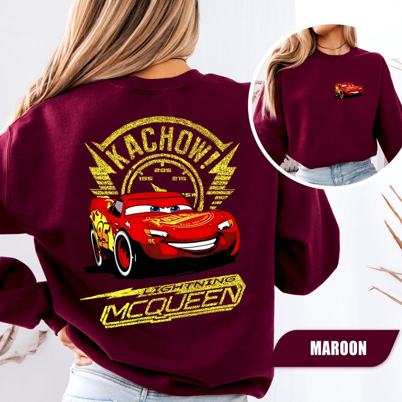 May include: A maroon long-sleeve sweatshirt featuring a large graphic on the back of the red race car Lightning McQueen with the text KACHOW and LIGHTNING MCQUEEN in yellow. A smaller version of the same red race car is printed on the front chest.