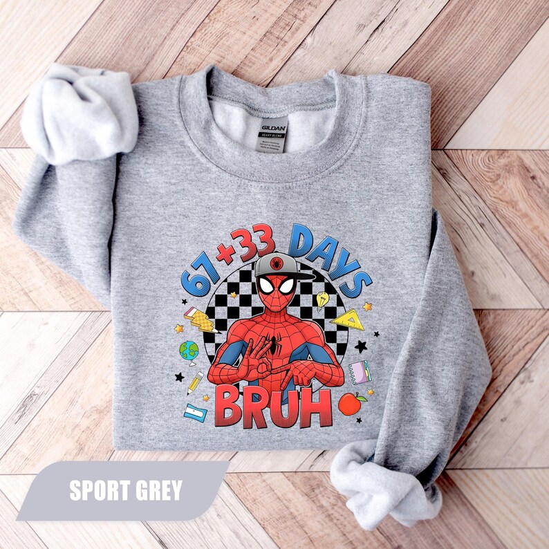 May include: Sport grey sweatshirt featuring a graphic of Spider-Man with the text "67+33 DAYS BRUH". The design includes a checkered background and various cartoon elements. The sweatshirt is made of a soft material.