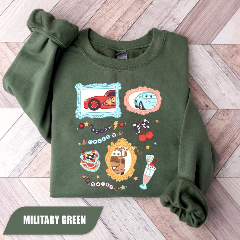 Puede incluir: Una sudadera de cuello redondo color verde militar con un estampado gr&aacute;fico de personajes de la pel&iacute;cula Cars. El dise&ntilde;o incluye im&aacute;genes enmarcadas de Rayo McQueen, Sally y Mate, junto a ilustraciones de un pastel, un batido y cerezas.