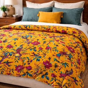 Peut inclure: Un lit avec une couverture jaune moutarde ornée d'un motif floral et d'oiseaux dans des tons de rose, de sarcelle et de violet. Le lit a des oreillers sarcelle et blancs, et une tête de lit en bois. Une lampe et une table de chevet sont visibles.