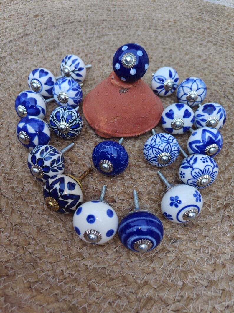 May include: A selection of ceramic cabinet knobs with blue and white patterns. The knobs display floral, polka dot, and striped designs. Each knob has a metal screw. The knobs are arranged on a woven surface, creating a decorative display.