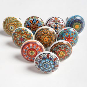 May include: A collection of ten decorative ceramic cabinet knobs. Each knob features a unique, colorful, and intricate pattern in shades of blue, orange, yellow, and red. The knobs have a round shape with a white base and metal hardware.