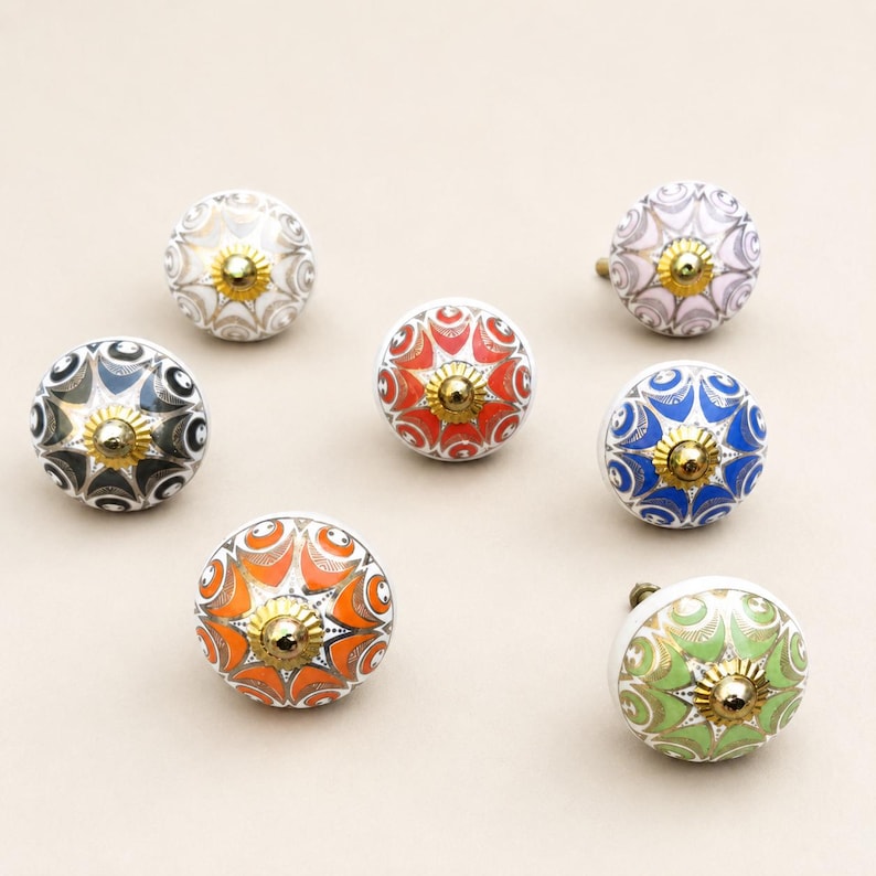 Pu&ograve; includere: Un set di sei pomelli rotondi in ceramica per mobili con intricati motivi floreali multicolori in arancione, blu, verde, nero e bianco. Ogni pomello &egrave; accentato con un elemento in metallo dorato al centro della parte superiore.