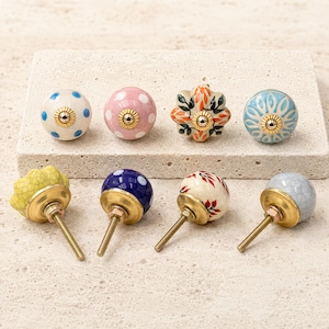 Pode incluir: Uma cole&ccedil;&atilde;o de oito puxadores decorativos para arm&aacute;rios com v&aacute;rios designs, incluindo bolinhas azuis sobre branco, bolinhas cor-de-rosa, padr&otilde;es florais laranja, desenhos radiais em azul e branco, verniz craquelado amarelo, bolinhas azuis, folhas vermelhas e craquelado cinzento.