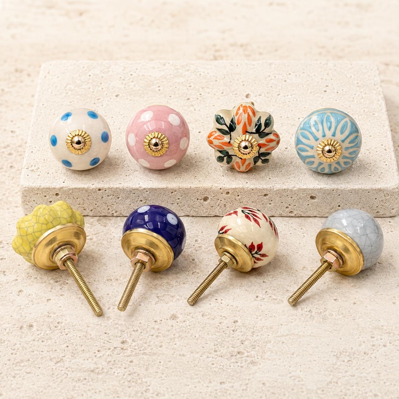 Pode incluir: Uma cole&ccedil;&atilde;o de oito puxadores decorativos para arm&aacute;rios com v&aacute;rios designs, incluindo bolinhas azuis sobre branco, bolinhas cor-de-rosa, padr&otilde;es florais laranja, desenhos radiais em azul e branco, verniz craquelado amarelo, bolinhas azuis, folhas vermelhas e craquelado cinzento.
