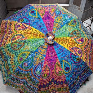 Puede incluir: Un paraguas abierto y colorido con un vibrante estampado de cachemira. El paraguas presenta una variedad de colores, incluyendo azul, verde, amarillo y rosa, con intrincados detalles bordados. El paraguas está diseñado para uso en exteriores.