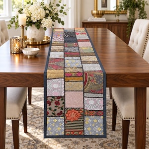 Puede incluir: Un camino de mesa rectangular con un diseño de patchwork compuesto por varios cuadrados de tela en diversos colores, incluyendo oro, rojo, gris y rosa, con intrincados patrones florales, geométricos y de cachemira, con un borde gris oscuro.
