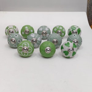 Pode incluir: Uma cole&ccedil;&atilde;o de puxadores de arm&aacute;rio de cer&acirc;mica decorativos em v&aacute;rios tons de verde e branco. Cada puxador apresenta um design pintado &uacute;nico, incluindo padr&otilde;es florais, cora&ccedil;&otilde;es e pontos. Os puxadores t&ecirc;m uma base de metal prateado.