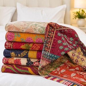 May include: A stack of six folded cotton quilts featuring various colorful patterns including floral, geometric, and botanical prints in shades of red, yellow, blue, and cream. Each quilt displays intricate kantha-style stitching throughout.