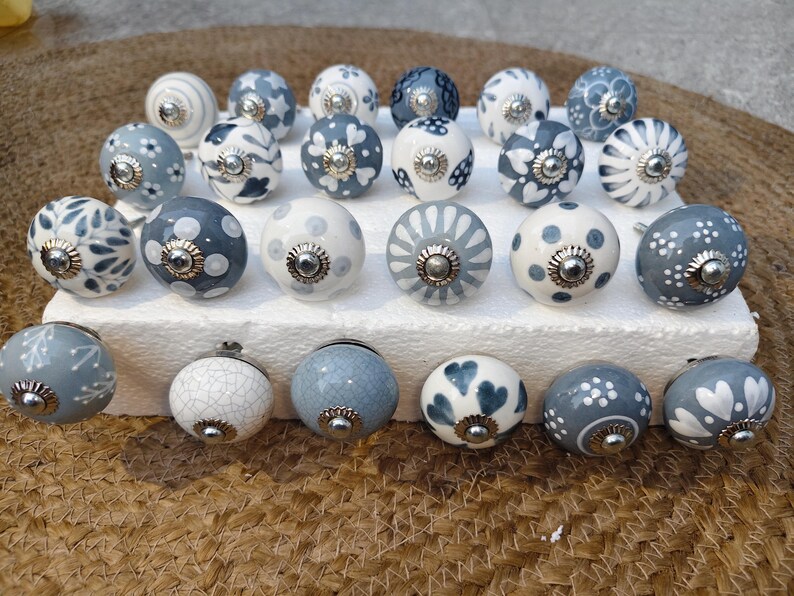 May include: A selection of ceramic cabinet knobs in blue and white. The knobs display diverse patterns, including floral and polka dots, with silver-coloured metal fixings. They are arranged on a white surface, offering a decorative touch.