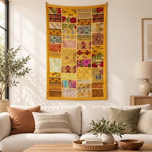 May include: A rectangular wall hanging featuring a patchwork design of various fabric squares in shades of yellow, gold, red, and green. The textile displays intricate embroidery, sequins, and floral patterns, finished with a solid yellow border.