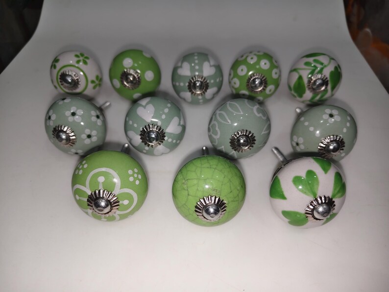 Pode incluir: Uma cole&ccedil;&atilde;o de puxadores de arm&aacute;rio decorativos em cer&acirc;mica, em tons de verde e branco. Os puxadores apresentam padr&otilde;es florais, de cora&ccedil;&atilde;o e de pontos, com ferragens met&aacute;licas prateadas. Ideais para adicionar um toque de charme aos m&oacute;veis.