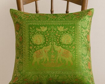 May include: A square green decorative pillow with an ornate gold elephant and floral pattern. The pillow is placed on a wooden chair. The pillow's design features two elephants facing each other.