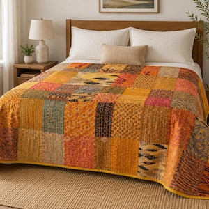 May include: A patchwork quilt featuring a variety of square fabric panels in shades of orange, yellow, brown, and muted red. The quilt displays diverse patterns including floral, geometric, and abstract prints, finished with a solid yellow border.