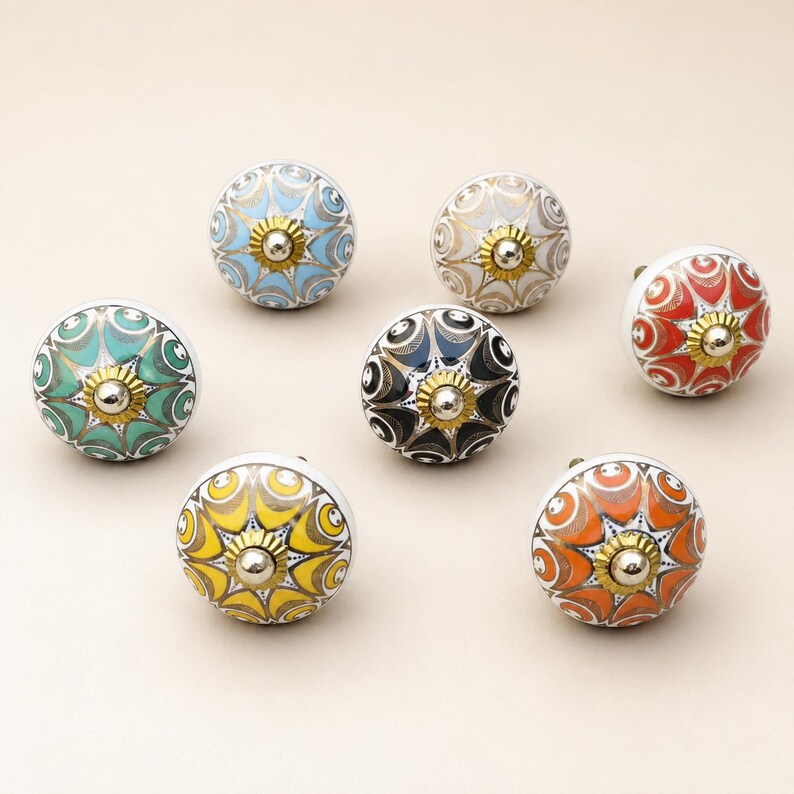 Pu&ograve; includere: Un set di sette pomelli rotondi in ceramica per mobili con intricati motivi di ispirazione floreale in vari colori tra cui azzurro, beige, rosso, verde, blu scuro, giallo e arancione, ciascuno con un elemento centrale in metallo dorato.