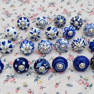 May include: A collection of twenty round ceramic cabinet knobs featuring various blue and white patterns, including floral, geometric, and polka dot designs. Each knob is finished with a central silver-toned metal hardware attachment.