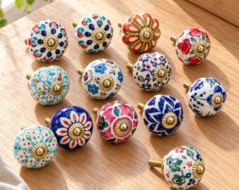 Può includere: Una collezione di dodici pomelli rotondi in ceramica per mobili con vari motivi floreali e geometrici dipinti a mano in colori vivaci tra cui blu, rosso, verde e arancione. Ogni pomello presenta una vite centrale in metallo color ottone.