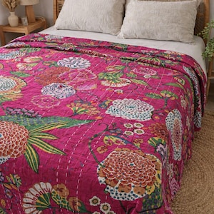 May include: A vibrant pink floral quilt with a large-scale botanical print. The quilt features a repeating pattern of colorful flowers and foliage, stitched with white thread. The bedspread is on a bed with neutral-colored pillows.