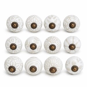 May include: A set of twelve round ceramic cabinet knobs arranged in three rows of four. Each knob features a white base with light grey embossed patterns and a central antique brass-coloured metal hardware piece with a fluted circular base.