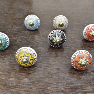 Pu&ograve; includere: Una collezione di sette pomelli rotondi in ceramica per mobili con intricati motivi geometrici in stile mandala multicolore nelle tonalit&agrave; del verde, blu, giallo, arancione, nero e bianco, ciascuno sormontato da un piccolo perno centrale dorato.