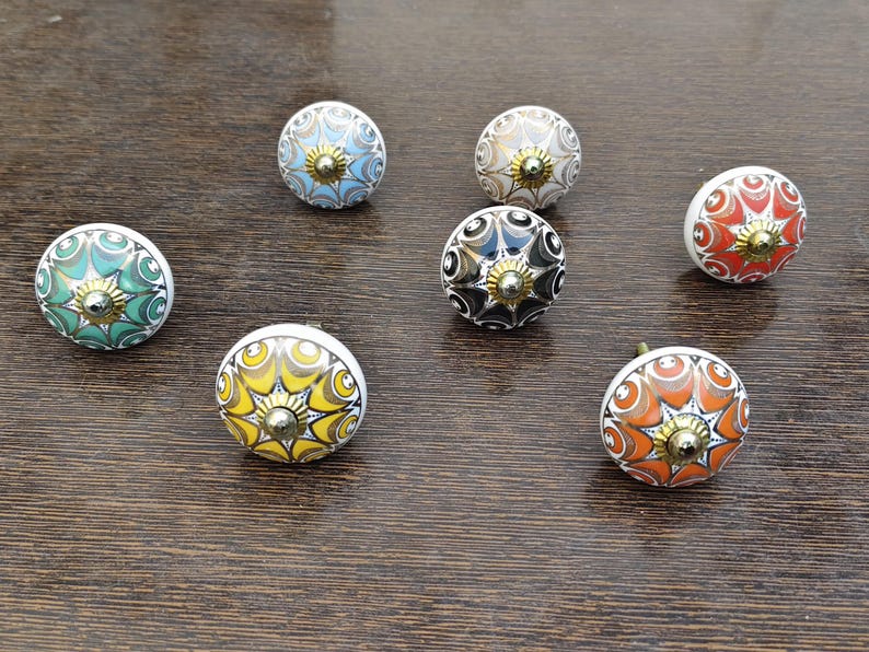 Pu&ograve; includere: Una collezione di sette pomelli rotondi in ceramica per mobili con intricati motivi geometrici in stile mandala multicolore nelle tonalit&agrave; del verde, blu, giallo, arancione, nero e bianco, ciascuno sormontato da un piccolo perno centrale dorato.