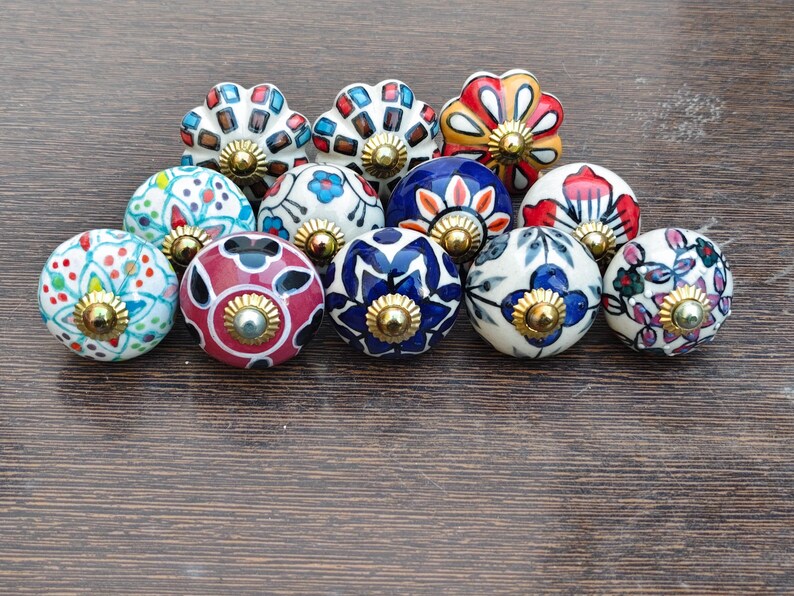 Pu&ograve; includere: Una collezione di undici pomelli decorativi in ceramica per armadi. I pomelli presentano vari motivi floreali e geometrici in colori come rosso, blu, bianco e verde. Ogni pomello ha una base in metallo dorato.