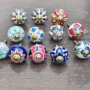 Pu&ograve; includere: Un set di tre tazze in ceramica con una glassa screziata color crema. Ogni tazza presenta un design dipinto a mano diverso: una foglia blu e verde, un fiore giallo e una bacca rossa. Le tazze hanno un design semplice e moderno.