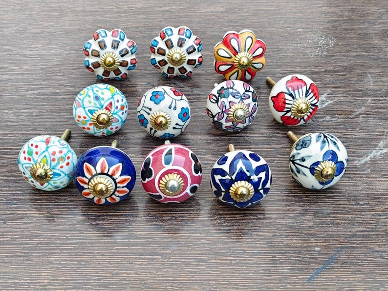 Pu&ograve; includere: Un set di tre tazze in ceramica con una glassa screziata color crema. Ogni tazza presenta un design dipinto a mano diverso: una foglia blu e verde, un fiore giallo e una bacca rossa. Le tazze hanno un design semplice e moderno.